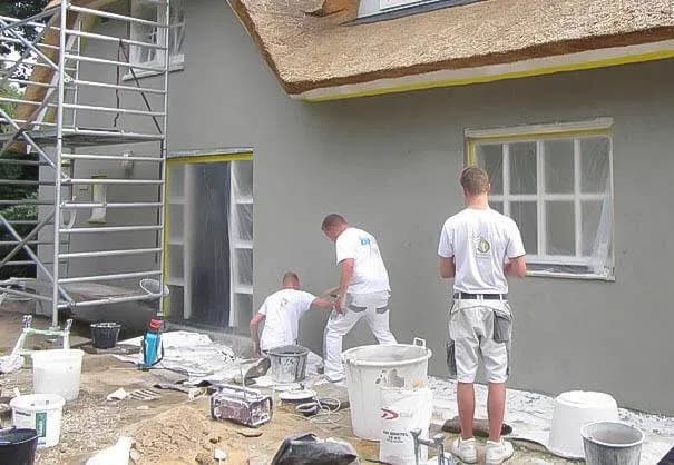 Stukadoors aan het werk aan de gevel van een woning met rieten dak