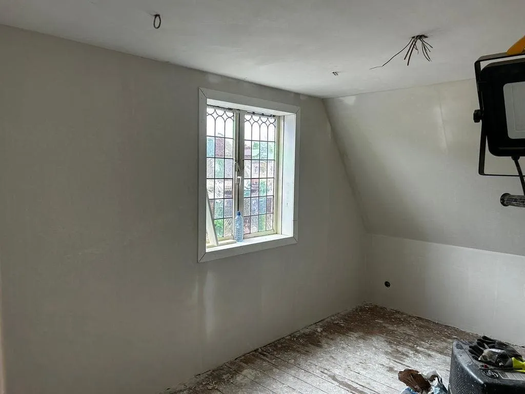 Zolderkamer met gestuukte schuine wand en glas-in-loodraam